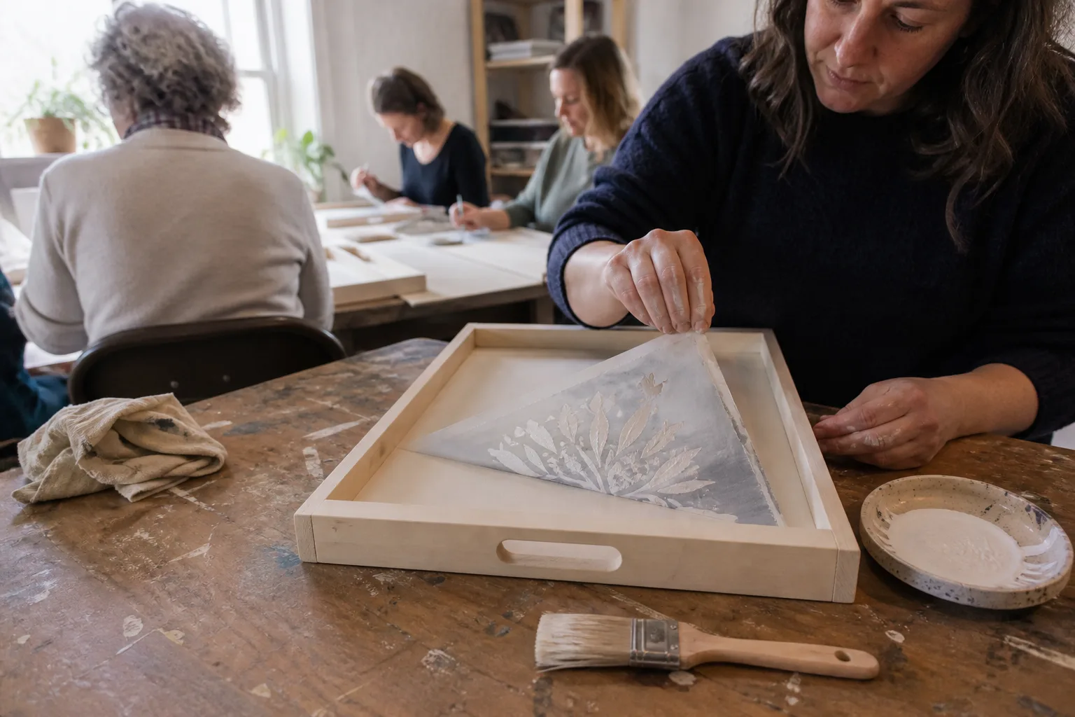 A stencil being lifted off a painted wooden tray
